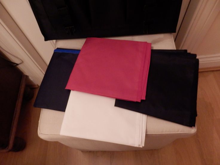 four different colored sheets sitting on top of a white chair next to a black bag