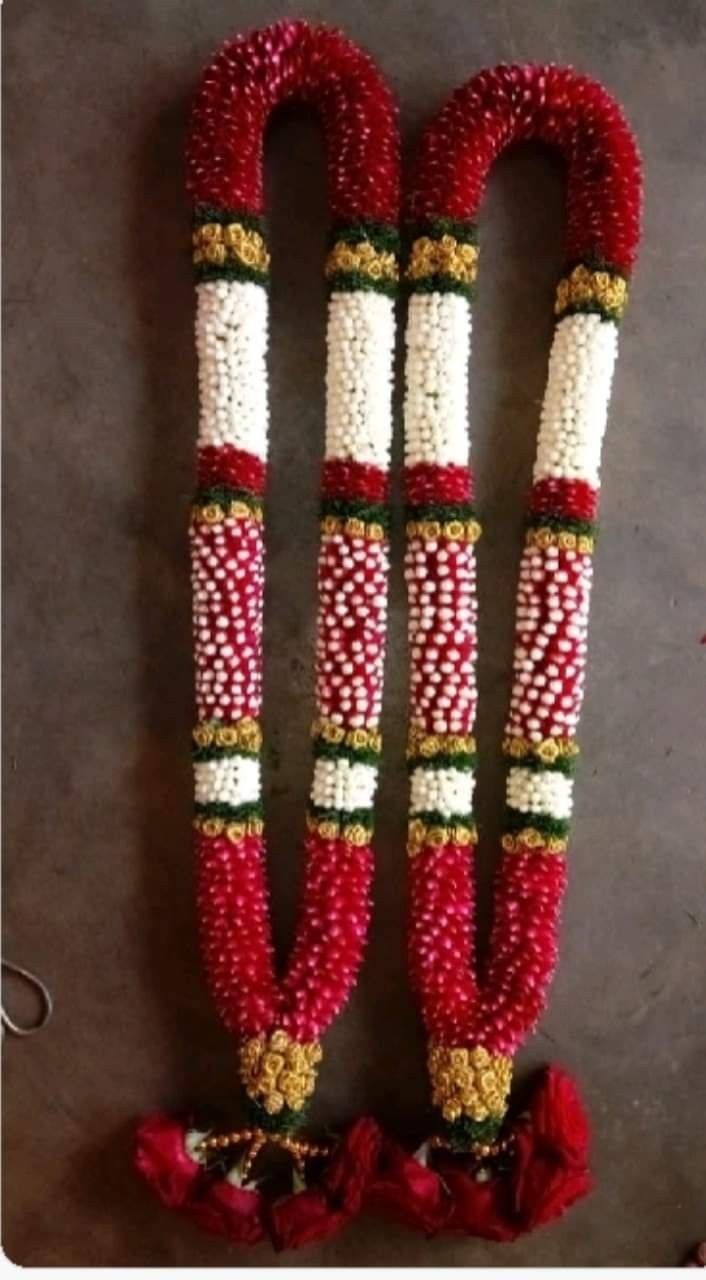 two red and white beaded garlands with flowers on the ground next to each other