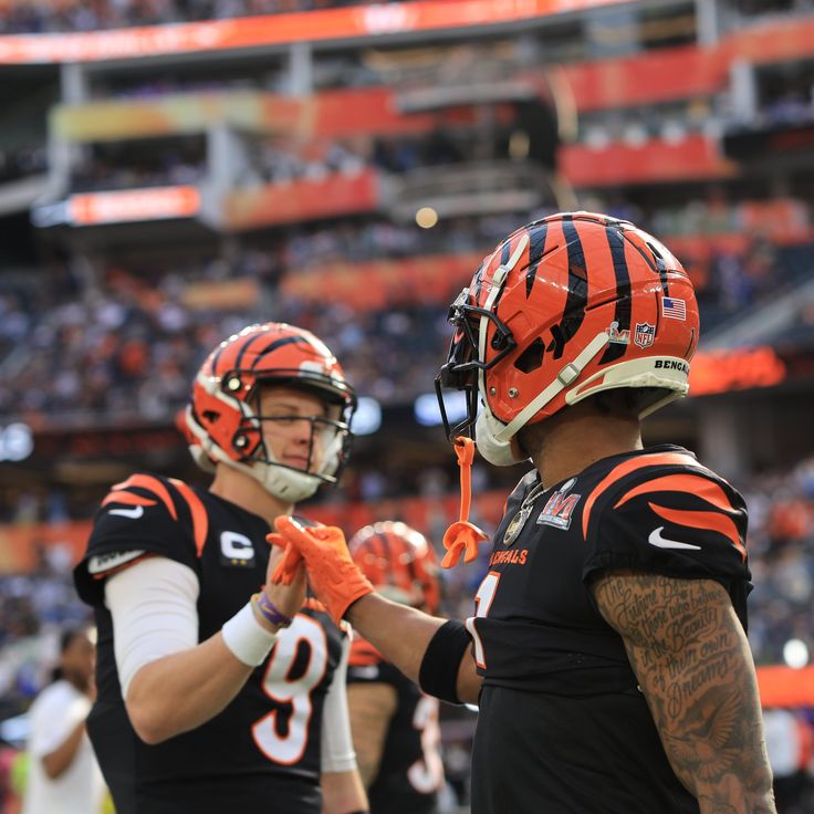 two football players shaking hands on the sidelines at an orange and black game with fans in the stands