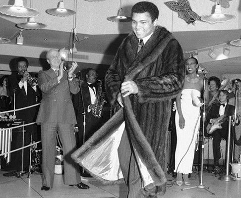 a man in a fur coat is dancing on the dance floor with other people watching