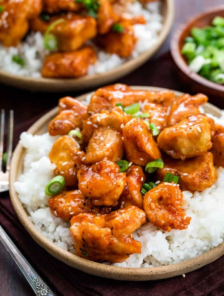 two plates filled with chicken and rice on top of a wooden table