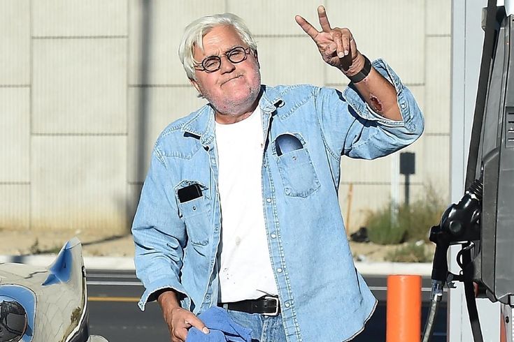 an older man giving the peace sign while standing in front of a gas station pump