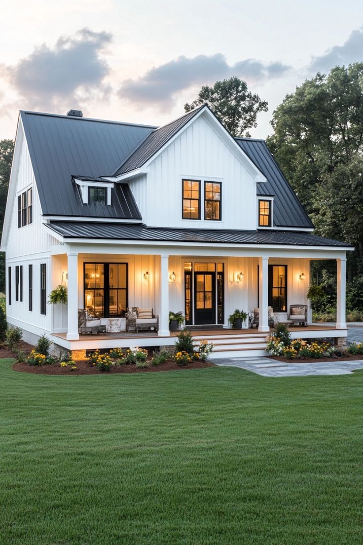 a large white house with black roof and windows on the front porch is lit up at night