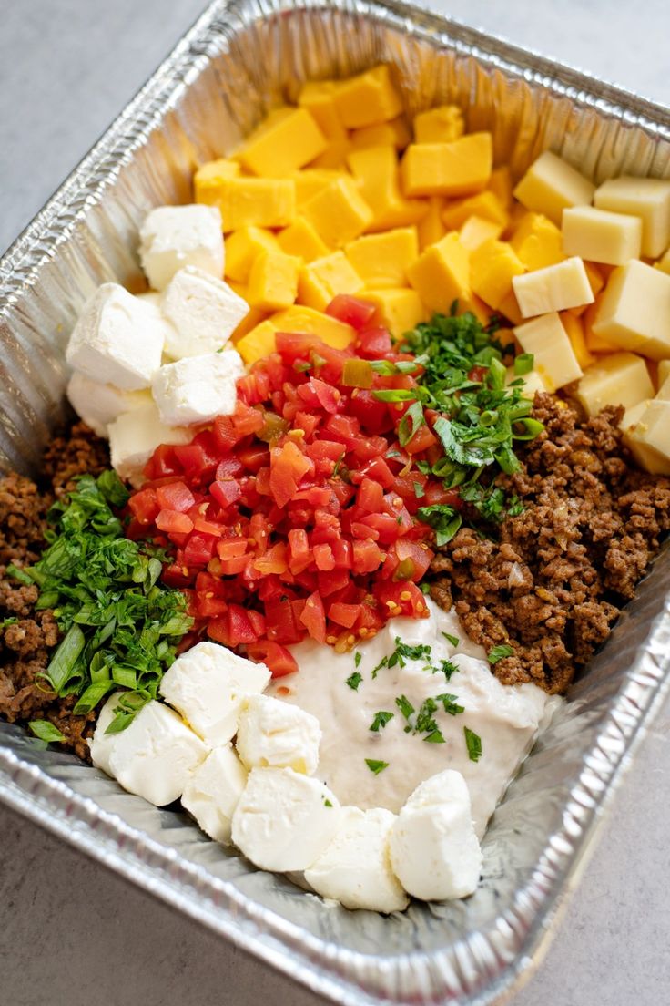 a metal pan filled with meat, cheese and veggies on top of a table