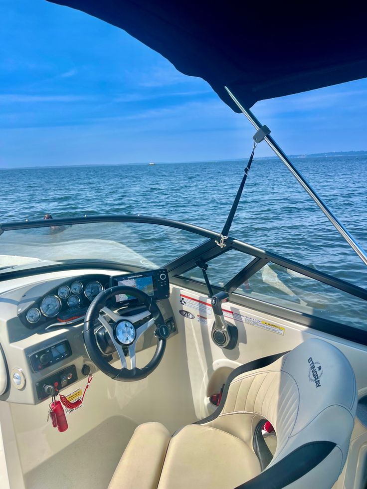 the inside of a boat with steering wheel and dash board on the water's edge