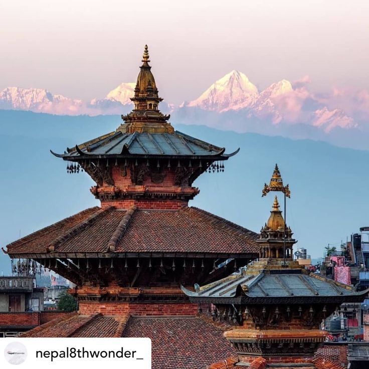 the top of two buildings with snow capped mountains in the backgrouds behind them