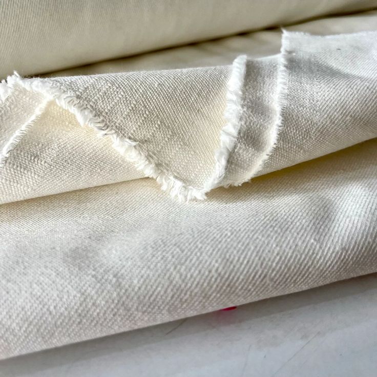 two white linens folded on top of each other, one with fraying edges