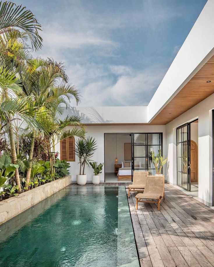 an outdoor swimming pool with lounge chairs and palm trees in the foreground, surrounded by greenery