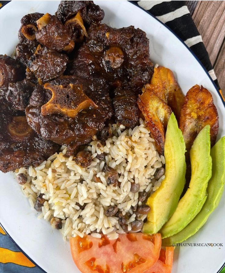 a white plate topped with meat and rice next to sliced avocado on a wooden table