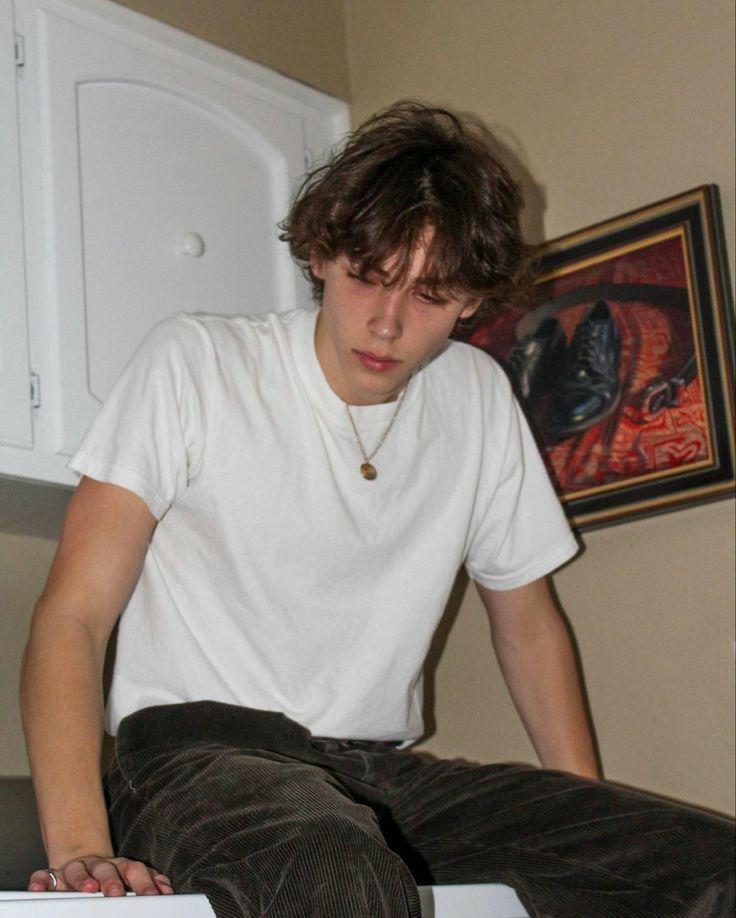 a young man sitting on top of a white refrigerator freezer next to a painting