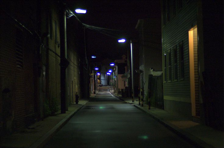 an empty alley at night with street lights and no cars on the road or sidewalks