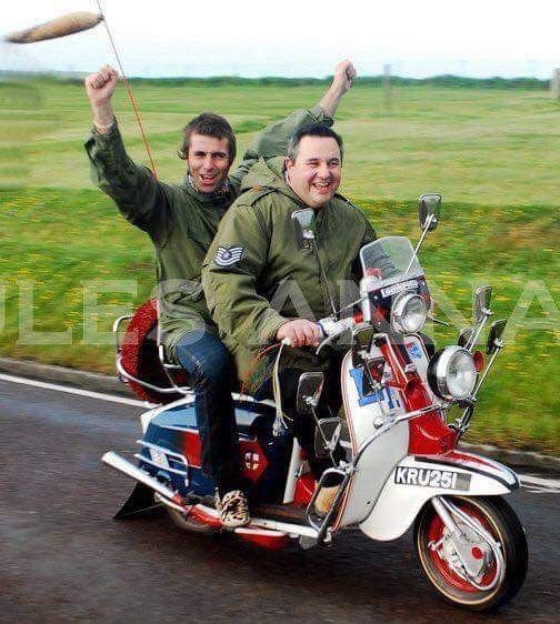 two men riding on the back of a motorcycle down a road with an object in the air