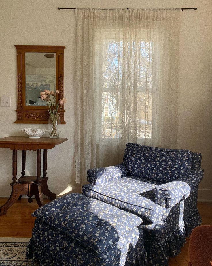 a living room with a chair and ottoman in front of a window that has sheer curtains