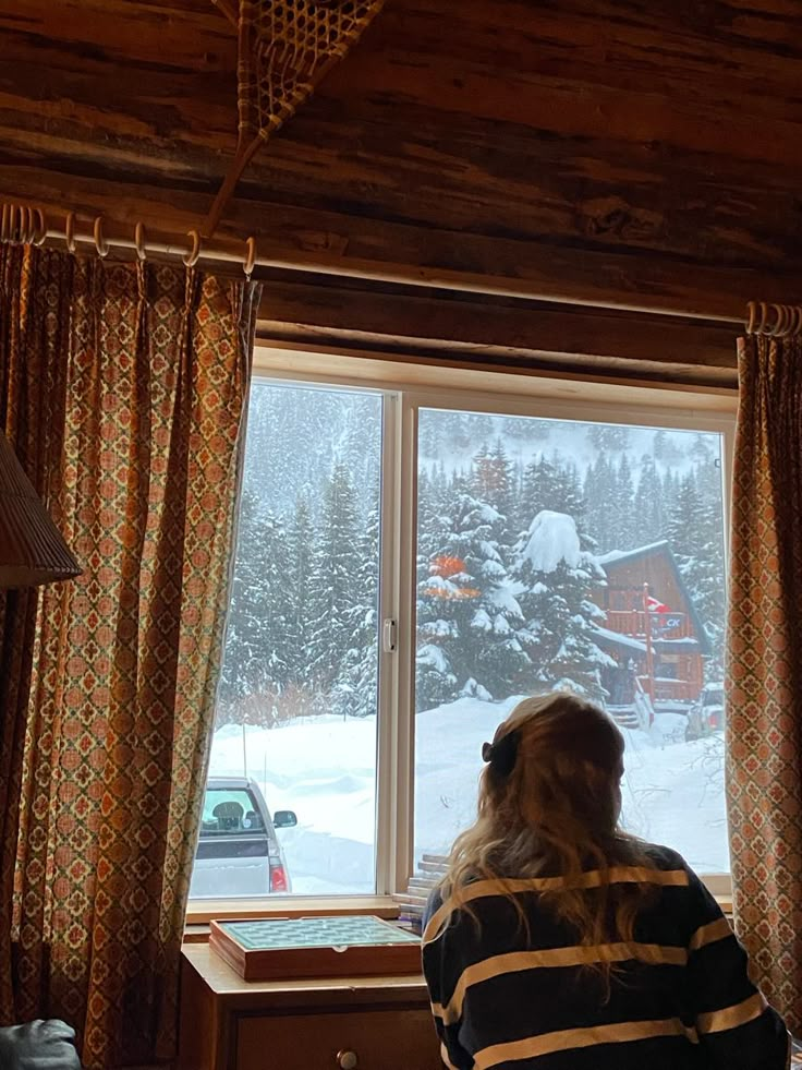 a woman is looking out the window at snow