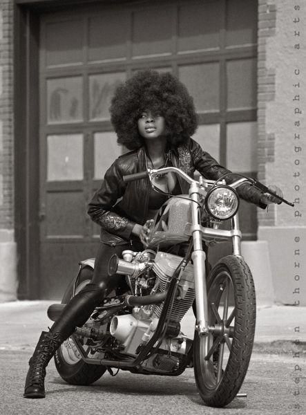 a black and white photo of a woman sitting on a motorcycle with an afro hairstyle