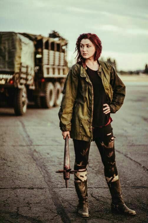 a woman standing in front of an army truck holding a bat and looking at the camera