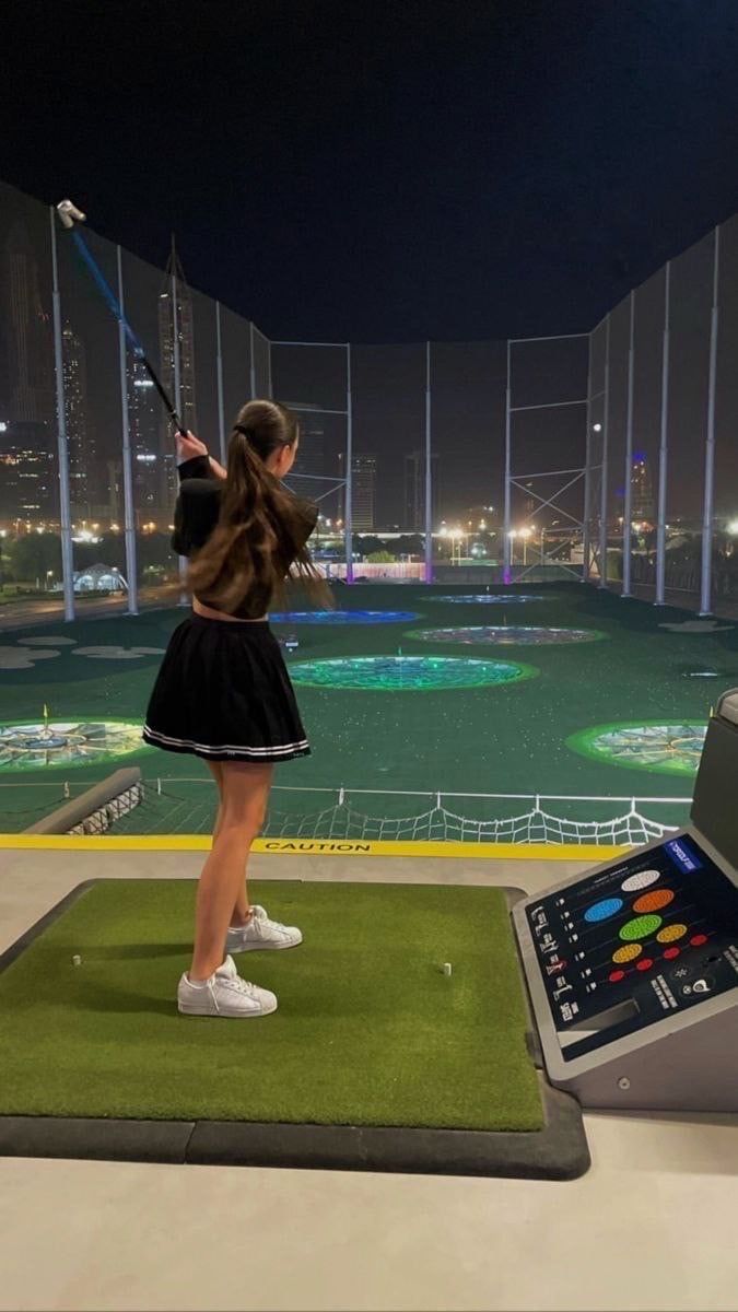 a woman in a black dress is playing golf on a green mat with a laptop