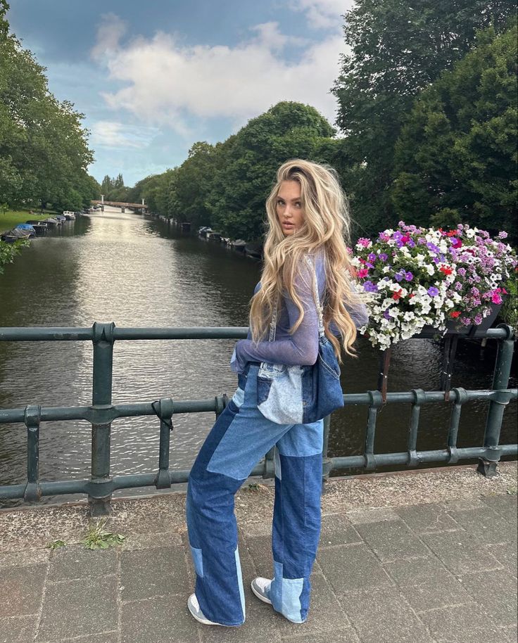 a woman standing on a bridge next to a body of water with flowers in the background