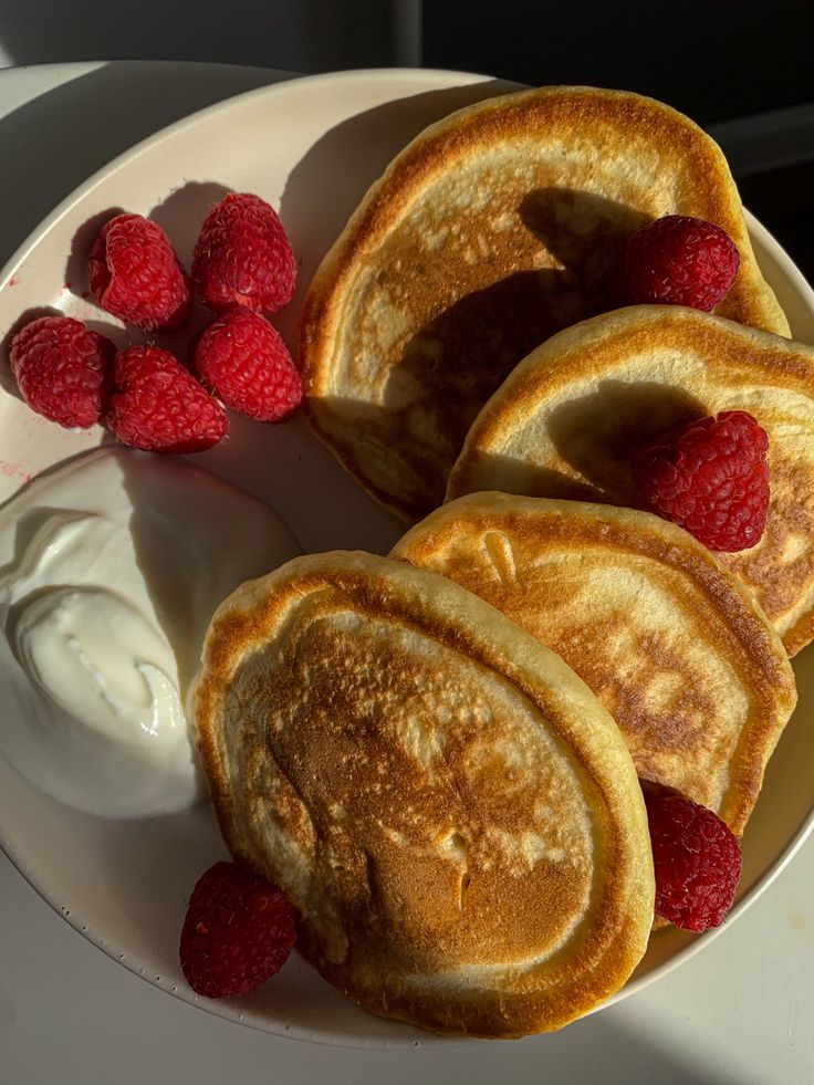 four pancakes on a plate with raspberries and yogurt