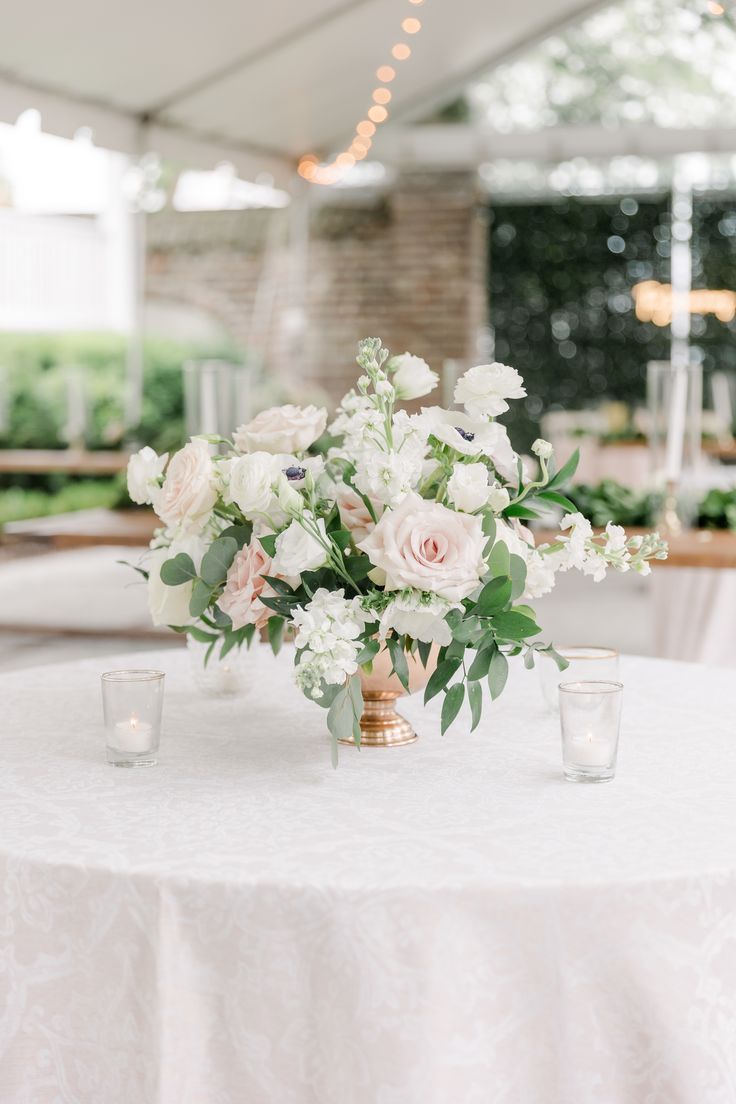 the centerpieces on this table are white and pink flowers with greenery in them