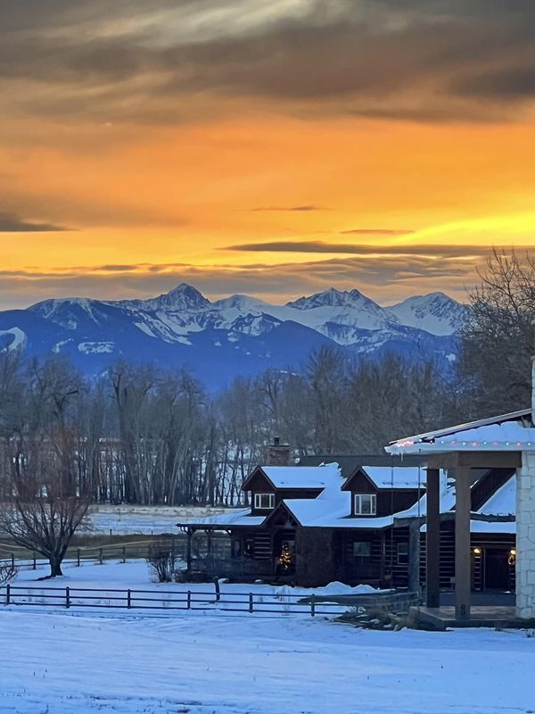 the mountains are covered in snow as the sun is setting over a barn and farm