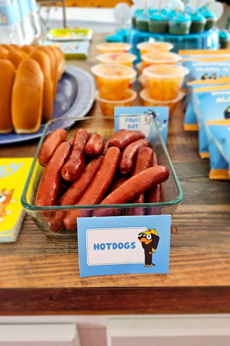 hotdogs are displayed in plastic containers on a table with other snacks and drinks