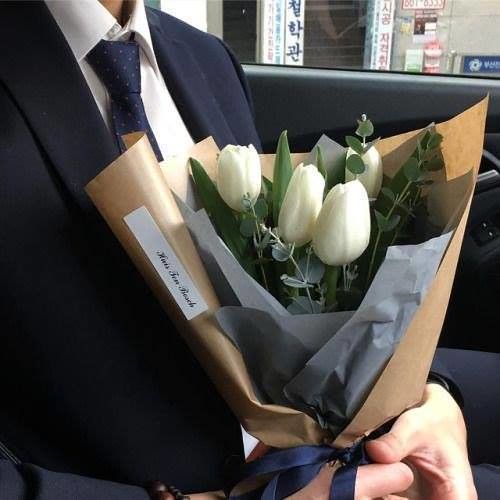 a man in a suit holding a bouquet of white tulips on his lap