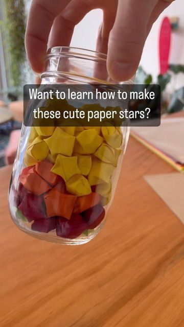 a person holding a jar filled with cut paper stars on top of a wooden table