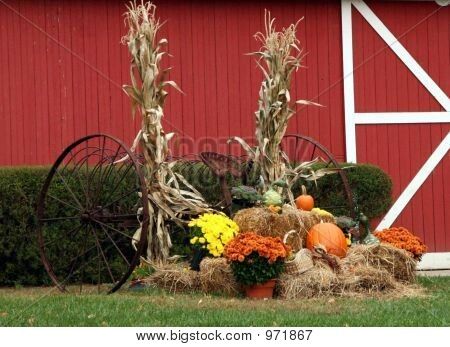 hay bales and pumpkins in front of a red barn with cornstalks