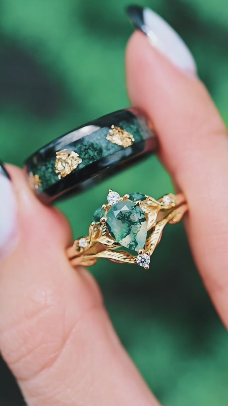 a woman's hand holding two rings with green stones