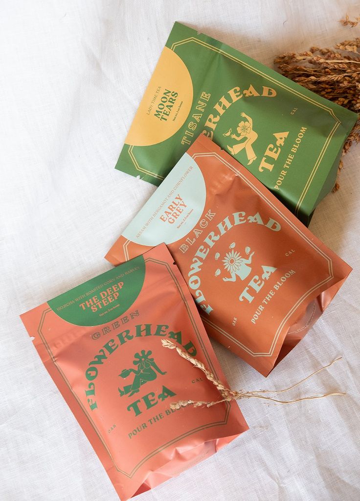 three bags of tea sitting on top of a white cloth covered bed next to dried grass