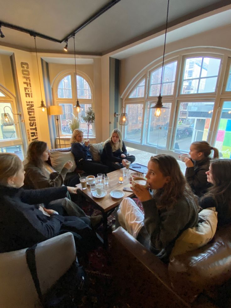 a group of people sitting around a living room table eating food and drinking coffee together