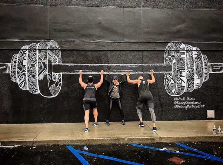 three people are doing exercises on the side of a building with their hands in the air