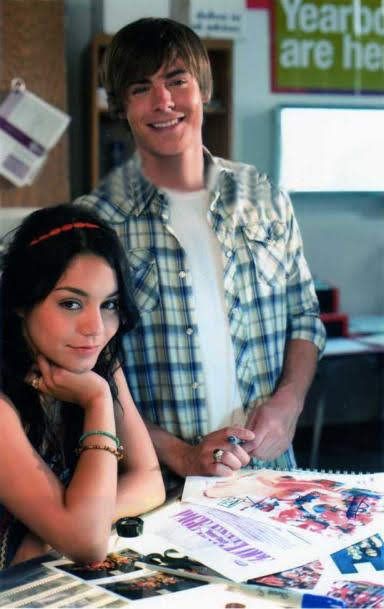 a young man standing next to a woman at a table with papers and magazines on it