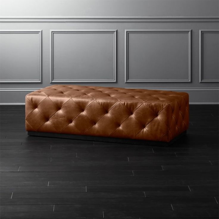 a brown leather bench sitting on top of a hard wood floor next to a wall