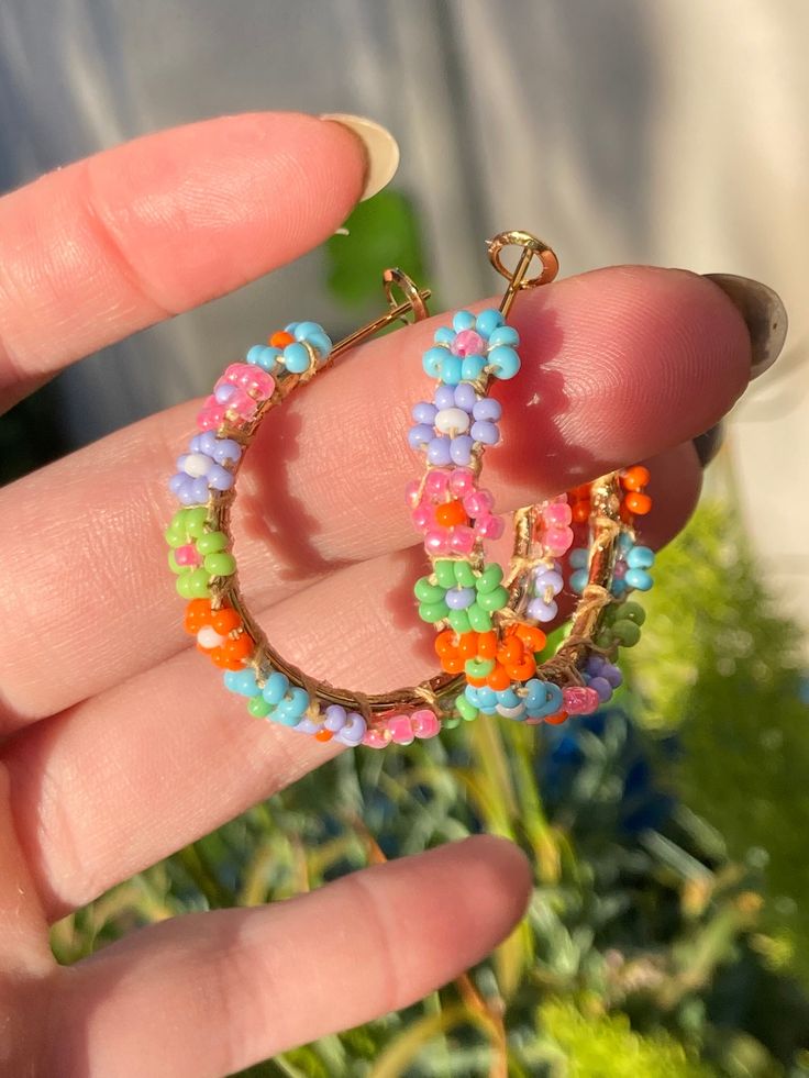 Handmade beaded hoop earrings 3.5 cm in diameter. The daisies are blue, pink, purple, green, and orange; perfect for spring or summer. They are lightweight, and the beads are mounted on a gold colored stainless steel hoop with a latch back closure. Beaded Earrings Hoop, Summer Tiny Beaded Small Hoop Earrings, Summer Tiny Beads Small Hoop Earrings, Beaded Hoop Earrings For Spring, Multicolor Beaded Flower Earrings For Spring, Spring Multicolor Beaded Flower Earrings, Trendy Flower Hoop Earrings For Summer, Spring Jewelry With Colorful Beads In Gold, Spring Gold Jewelry With Colorful Beads