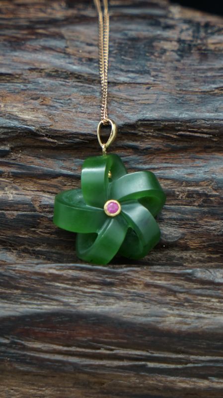 a green flower shaped pendant on a gold plated chain with a pink stone in the center