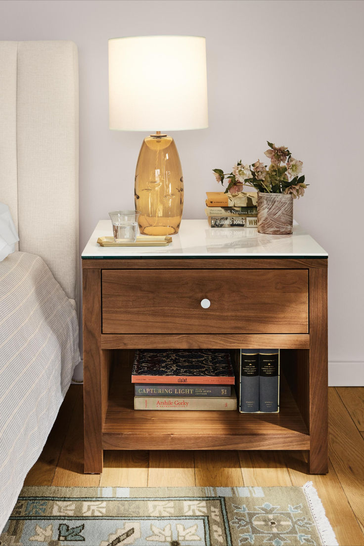 a nightstand with a lamp on top of it next to a bed