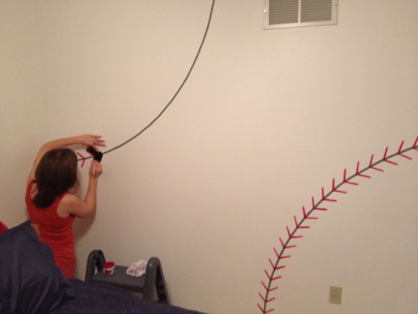 a woman in a red shirt is playing with a baseball ball on the wall next to her bed