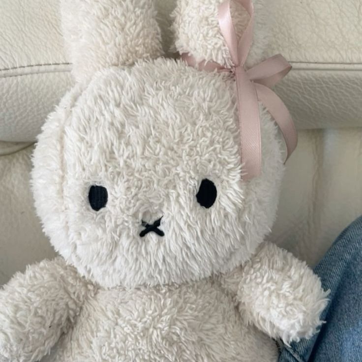 a white stuffed animal with a pink bow on its head sitting in someone's lap