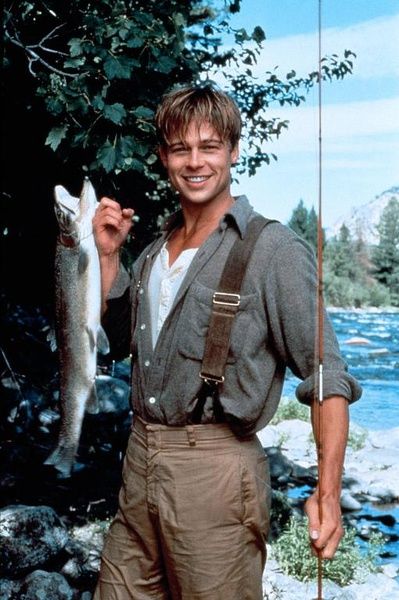 a man holding a fish while standing in front of a river with rocks and trees