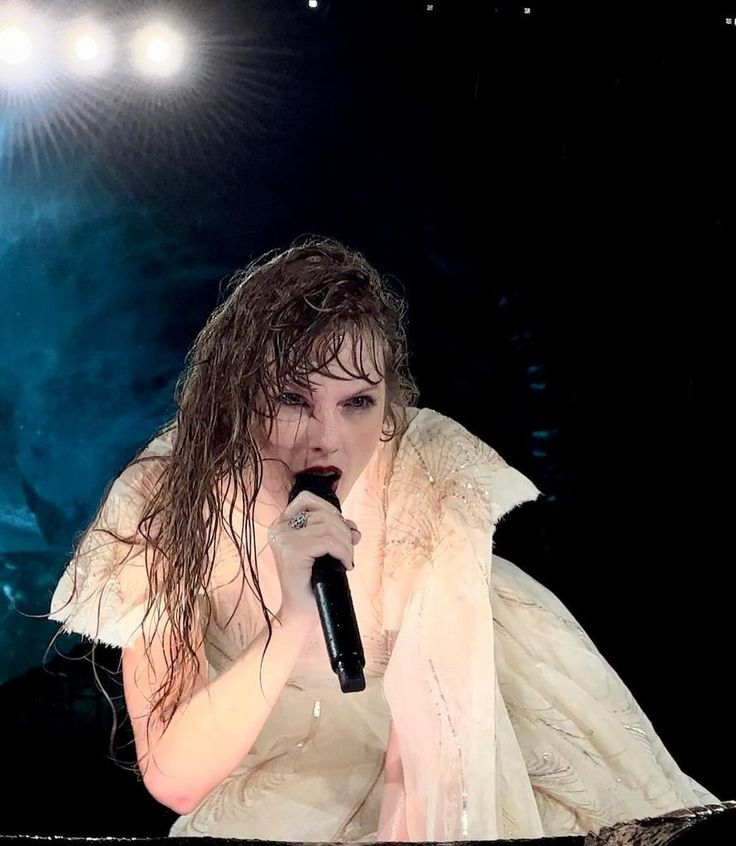 a woman with wet hair holding a microphone in front of a stage light and wearing a white dress