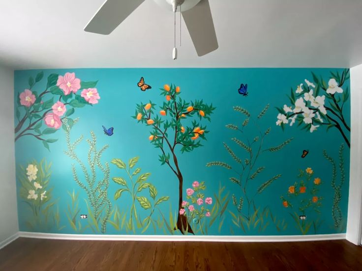 an empty room with blue walls and flowers painted on the wall next to a ceiling fan