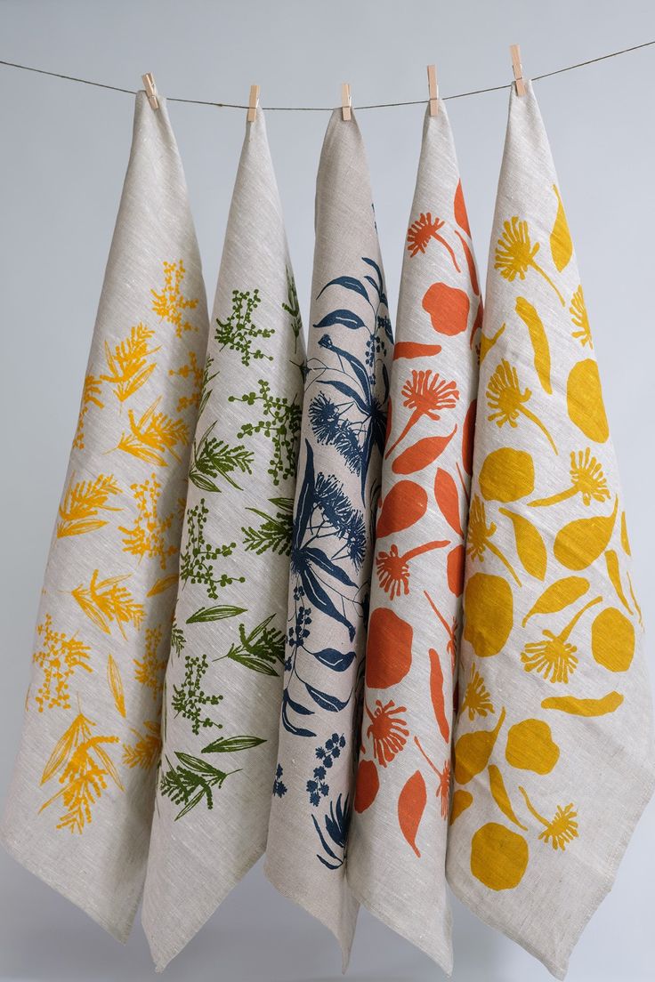 four tea towels hanging from a clothes line with different designs on them, all in various colors