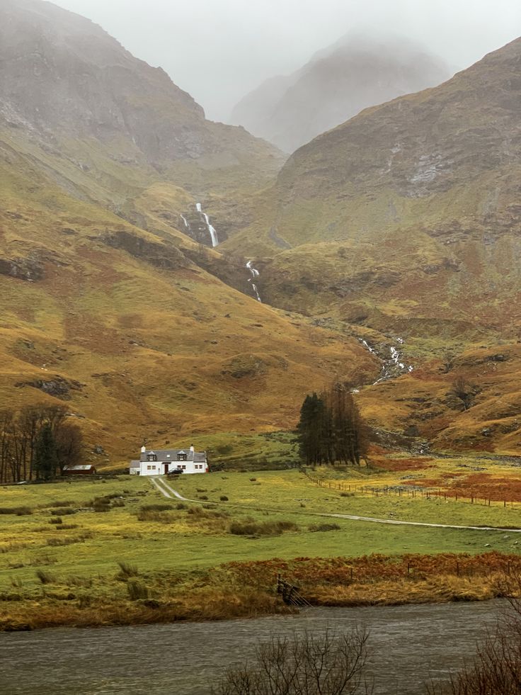 a house in the middle of a valley with mountains in the backgrouds