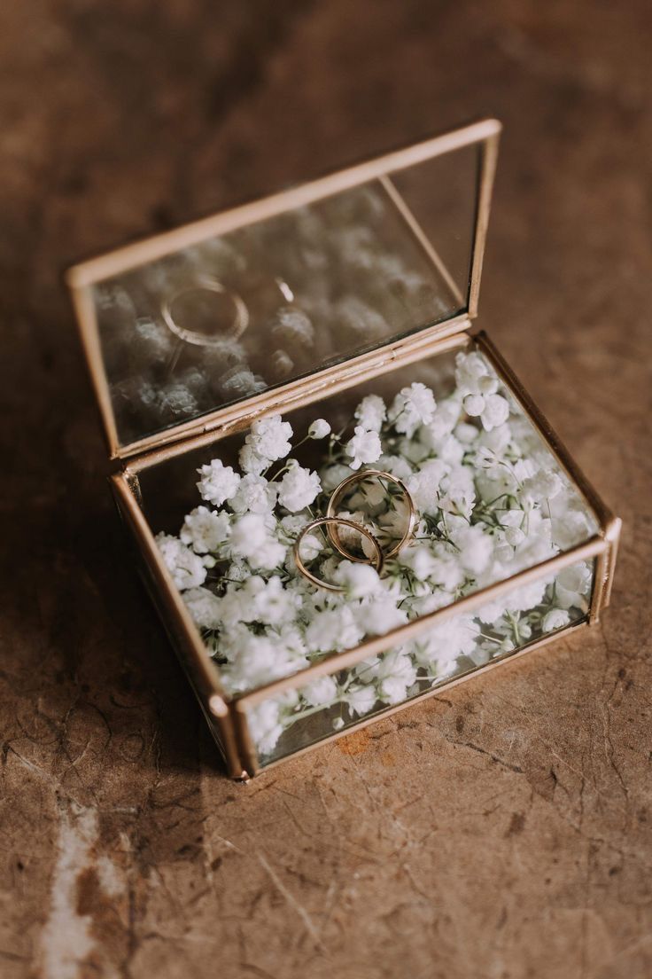 two wedding rings sitting in a box filled with white flowers on the floor next to each other