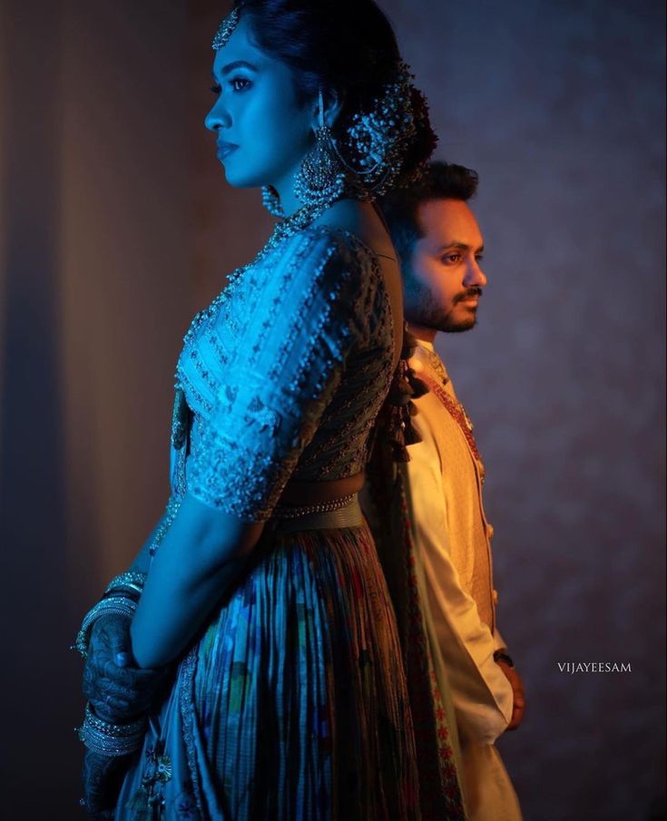 a man and woman standing next to each other in front of a dark background with blue light