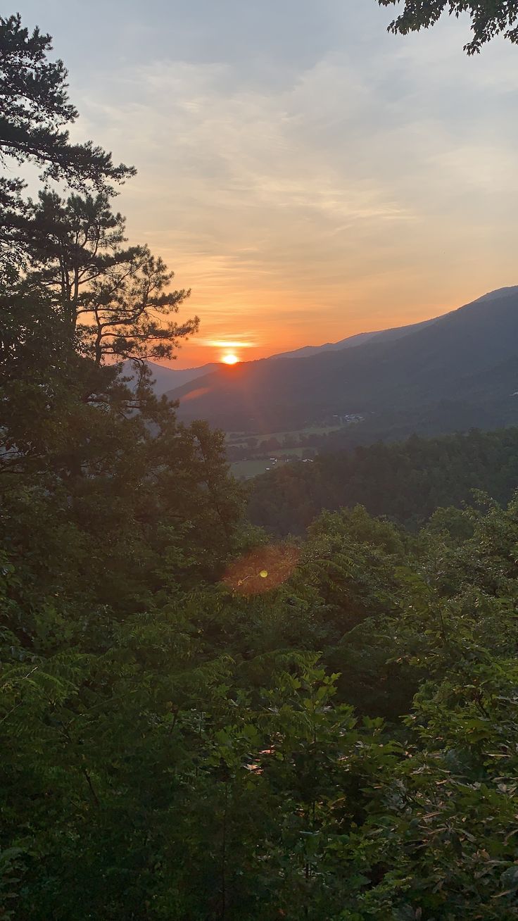 the sun is setting over some trees and mountains