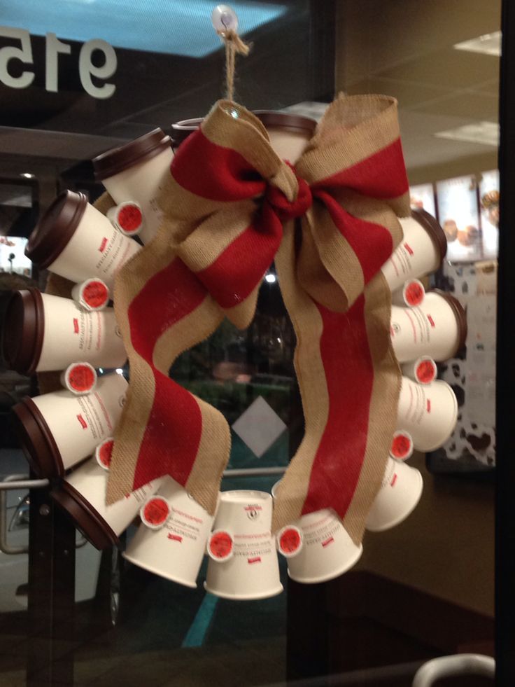 a christmas wreath with coffee cups hanging from it's front door, decorated with red and tan ribbon