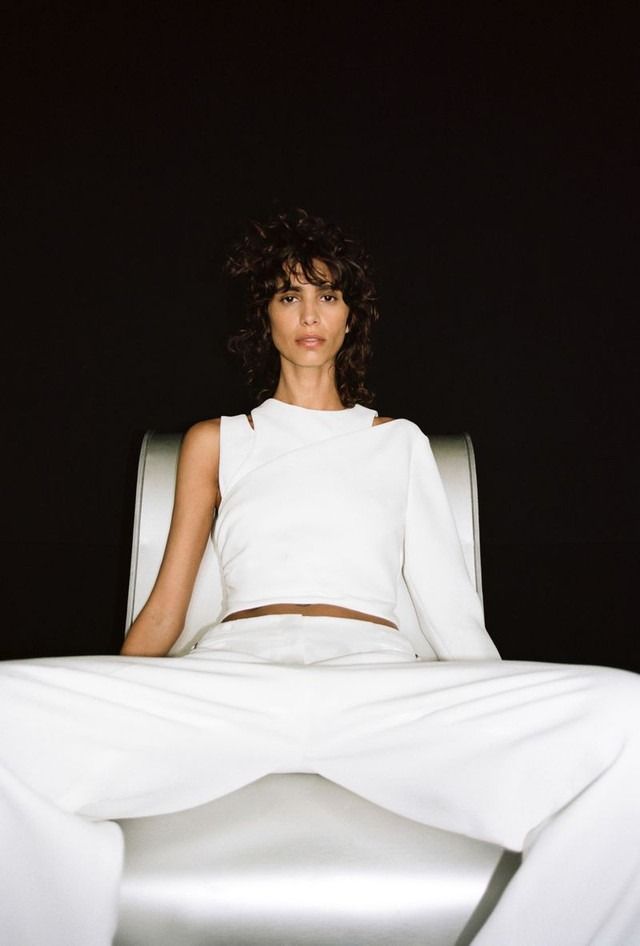 a woman sitting in a white chair with her legs crossed and looking at the camera